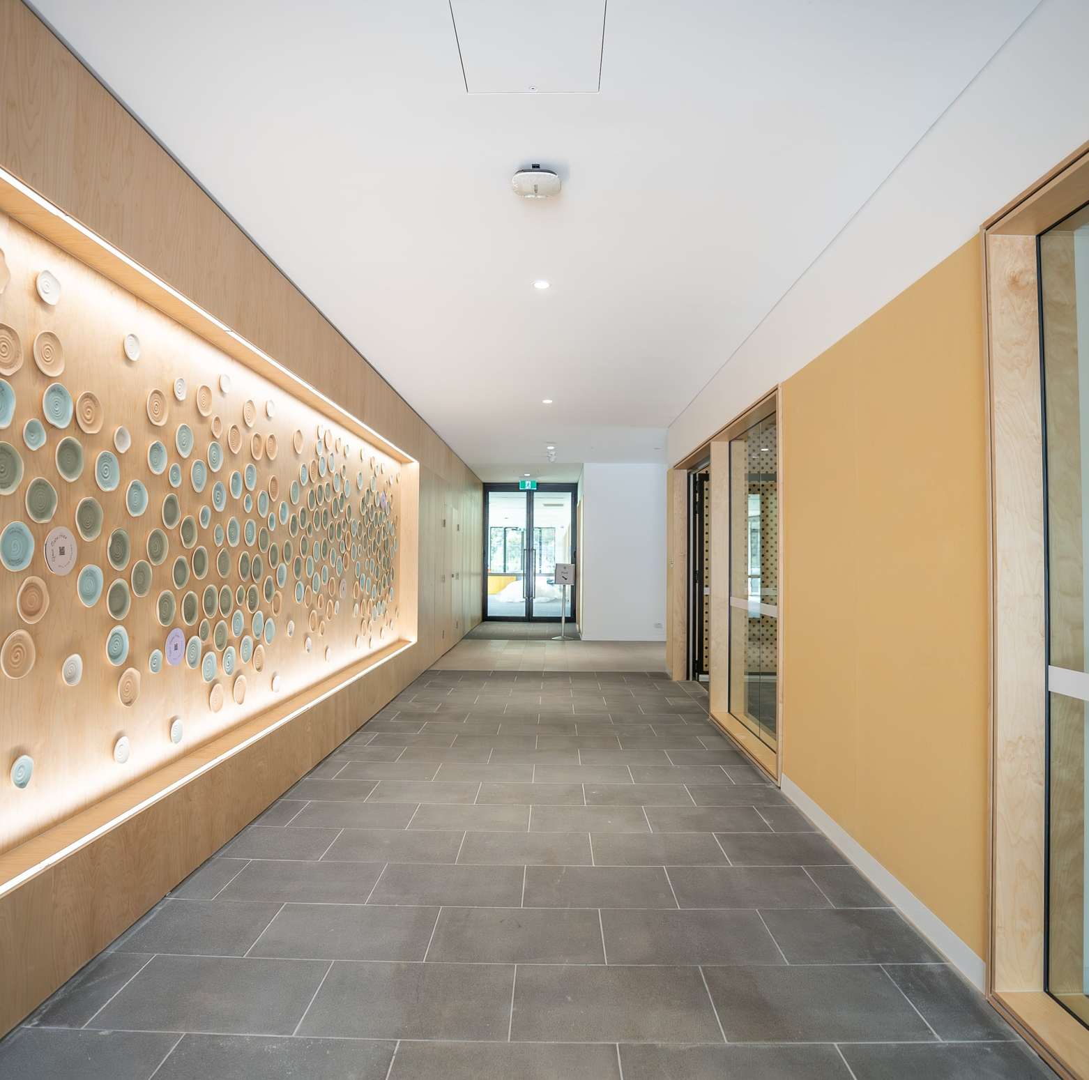 A corridor with a decorative ceramic wall installation, lit by DALI-2 controlled downlights